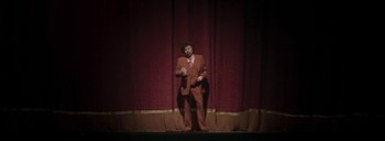 Movie still from “Post Mortem” (2010), directed by Pablo Larraín – A man standing on a stage with a microphone in his hand; Wide shot, Low angle