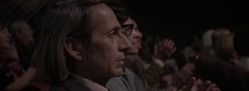 Movie still from “Post Mortem” (2010), directed by Pablo Larraín – Two men sitting in front of each other in front of an audience; Close Up shot, Over the shoulder angle