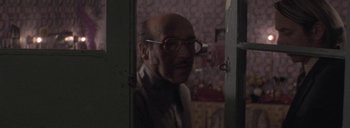 Movie still from “Post Mortem” (2010), directed by Pablo Larraín – An old man with glasses is standing in a room; Close Up shot, Over the shoulder angle