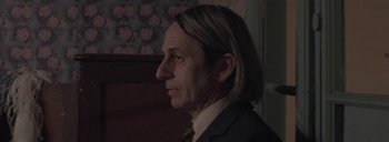 Movie still from “Post Mortem” (2010), directed by Pablo Larraín – A person wearing a suit and tie; Close Up shot, Over the shoulder angle