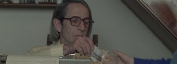 Movie still from “Post Mortem” (2010), directed by Pablo Larraín – An older man with glasses is eating something; Close Up shot, Over the shoulder angle
