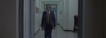 Movie still from “Post Mortem” (2010), directed by Pablo Larraín – A man in a suit and tie walking down a hall way; Medium shot, Low angle