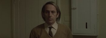Movie still from “Post Mortem” (2010), directed by Pablo Larraín – A man with long blonde hair wearing a tie; Close Up shot, Over the shoulder angle