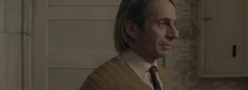 Movie still from “Post Mortem” (2010), directed by Pablo Larraín – A person with long hair wearing a tie; Close Up shot, Over the shoulder angle
