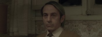 Movie still from “Post Mortem” (2010), directed by Pablo Larraín – A person wearing a suit and tie; Close Up shot, High angle