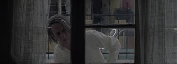 Movie still from “Post Mortem” (2010), directed by Pablo Larraín – A woman looking out of a window in a room; Close Up shot, Over the shoulder angle