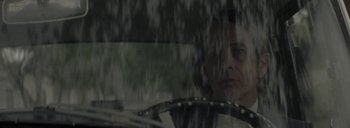 Movie still from “Post Mortem” (2010), directed by Pablo Larraín – A man sitting in the drivers seat of a car in the rain; Close Up shot, Low angle