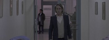 Movie still from “Post Mortem” (2010), directed by Pablo Larraín – A man in a suit and tie standing in front of a door; Medium shot, Over the shoulder angle
