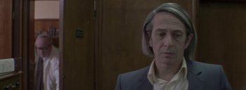 Movie still from “Post Mortem” (2010), directed by Pablo Larraín – A man with long hair and a suit and tie; Close Up shot, Low angle