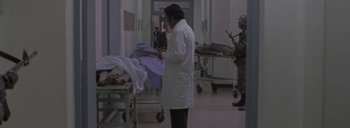 Movie still from “Post Mortem” (2010), directed by Pablo Larraín – A man in a white lab coat standing next to a bed; Wide shot, Over the shoulder angle
