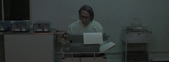 Movie still from “Post Mortem” (2010), directed by Pablo Larraín – A man in a white shirt is typing on a typewriter; Medium shot, Low angle