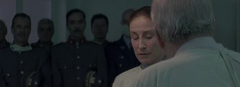 Movie still from “Post Mortem” (2010), directed by Pablo Larraín – A woman in a white shirt is standing in front of a group of men; Close Up shot, Over the shoulder angle