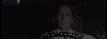 Movie still from “Post Mortem” (2010), directed by Pablo Larraín – A man sitting in the drivers seat of a car at night; Close Up shot, Low angle