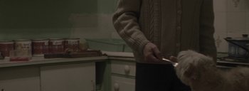 Movie still from “Post Mortem” (2010), directed by Pablo Larraín – A person holding a cigarette in a kitchen; Medium shot, High angle