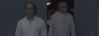 Movie still from “Post Mortem” (2010), directed by Pablo Larraín – Two men in white lab coats standing in a room; Medium shot, Low angle