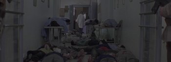 Movie still from “Post Mortem” (2010), directed by Pablo Larraín – A group of people in a room with beds and blankets; Wide shot, High angle