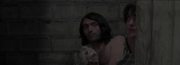 Movie still from “Post Mortem” (2010), directed by Pablo Larraín – A man with long black hair is holding a dog; Medium shot, Low angle