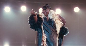 Movie still from “Precious” (2009), directed by Lee Daniels – A woman is singing on a stage with lights in the background; Medium shot, Low angle