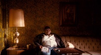Movie still from “Precious” (2009), directed by Lee Daniels – A man sitting on a couch holding a cassette tape; Medium shot, High angle