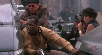 Movie still from “Predator 2” (1990), directed by Stephen Hopkins – A group of men sitting next to each other on the street; Medium shot, Over the shoulder angle