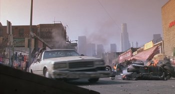 Movie still from “Predator 2” (1990), directed by Stephen Hopkins – A white car driving down a street next to buildings; Extreme Wide shot, High angle