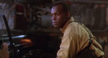 Movie still from “Predator 2” (1990), directed by Stephen Hopkins – A man in a yellow shirt is sitting down; Close Up shot, Low angle