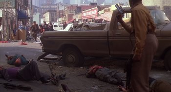 Movie still from “Predator 2” (1990), directed by Stephen Hopkins – A man laying on the ground in front of a truck; Wide shot, High angle