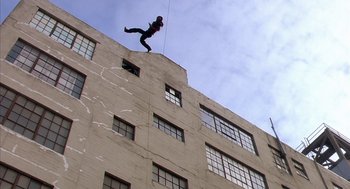 Movie still from “Predator 2” (1990), directed by Stephen Hopkins – A man on a rope attached to the side of a building; Extreme Wide shot, Low angle
