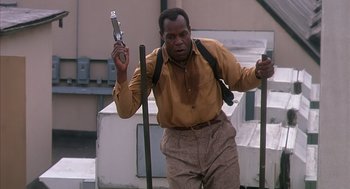 Movie still from “Predator 2” (1990), directed by Stephen Hopkins – A man in a brown shirt holding an object; Medium shot, Low angle