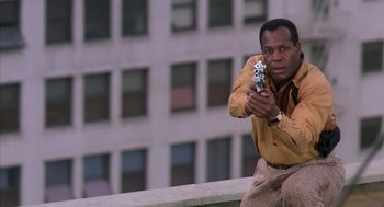 Movie still from “Predator 2” (1990), directed by Stephen Hopkins – A man holding a cell phone while sitting on a ledge; Medium shot, Low angle
