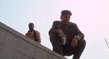 Movie still from “Predator 2” (1990), directed by Stephen Hopkins – Two men are sitting on a ledge and one is holding a bottle; Medium shot, Low angle