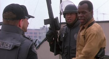 Movie still from “Predator 2” (1990), directed by Stephen Hopkins – A man holding a gun in front of two other men; Medium shot, Over the shoulder angle