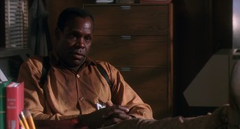 Movie still from “Predator 2” (1990), directed by Stephen Hopkins – A man sitting on a bed in front of a wooden dresser; Close Up shot, Low angle