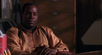 Movie still from “Predator 2” (1990), directed by Stephen Hopkins – A man sitting in front of a wooden wall; Close Up shot, Low angle