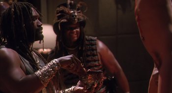 Movie still from “Predator 2” (1990), directed by Stephen Hopkins – A man in a costume is drinking from a cup; Medium shot, Over the shoulder angle