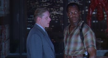 Movie still from “Predator 2” (1990), directed by Stephen Hopkins – Two men standing next to each other in front of a building; Medium shot, Low angle