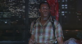 Movie still from “Predator 2” (1990), directed by Stephen Hopkins – A man in plaid shirt and suspenders standing in front of a building; Medium shot, Low angle