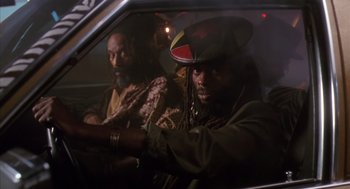 Movie still from “Predator 2” (1990), directed by Stephen Hopkins – A man in a hat sitting in the back seat of a car; Medium shot, Low angle