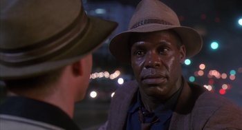 Movie still from “Predator 2” (1990), directed by Stephen Hopkins – A man wearing a hat talking to another man in a suit; Close Up shot, Over the shoulder angle