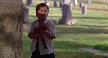Movie still from “Predator 2” (1990), directed by Stephen Hopkins – A young boy holding a bouquet of flowers in a cemetery; Medium shot, Over the shoulder angle