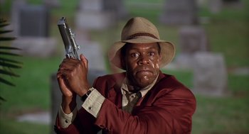 Movie still from “Predator 2” (1990), directed by Stephen Hopkins – A man in a hat and a suit holding a gun; Close Up shot, Low angle