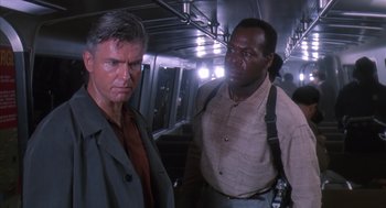 Movie still from “Predator 2” (1990), directed by Stephen Hopkins – Two men standing next to each other on a train; Medium shot, Low angle