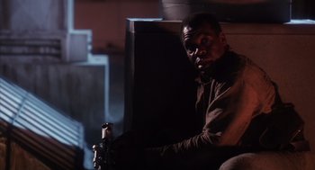 Movie still from “Predator 2” (1990), directed by Stephen Hopkins – A man sitting in front of a tv in a dark room; Medium shot, Low angle