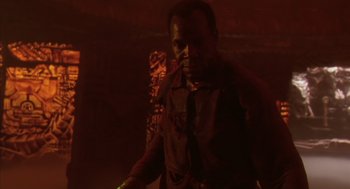 Movie still from “Predator 2” (1990), directed by Stephen Hopkins – A man standing in the dark holding a green object; Medium shot, Low angle