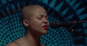 A woman with a shaved head singing into a microphone
