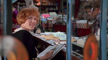 Movie still from “Pretty in Pink” (1986), directed by Howard Deutch – A woman sitting in front of a table with papers on top of it; Medium shot, Over the shoulder angle
