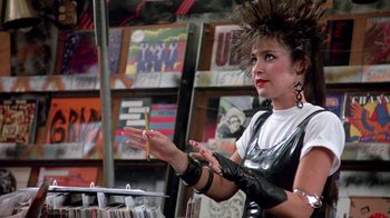 Movie still from “Pretty in Pink” (1986), directed by Howard Deutch – A woman in a black and white outfit holding a pencil; Medium shot, Over the shoulder angle