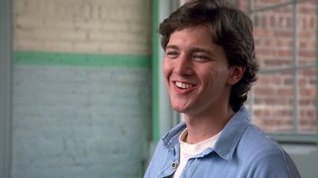 Movie still from “Pretty in Pink” (1986), directed by Howard Deutch – A young man smiling for the camera in front of a brick wall; Close Up shot, Low angle