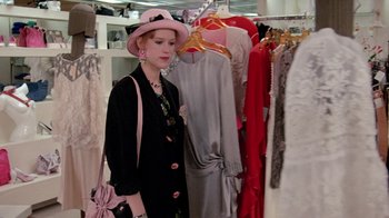Movie still from “Pretty in Pink” (1986), directed by Howard Deutch – A woman in a pink hat is standing in front of a rack of dresses; Medium shot, Over the shoulder angle