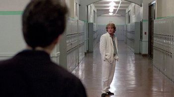 Movie still from “Pretty in Pink” (1986), directed by Howard Deutch – A man in a white suit standing in the hallway of a school; Wide shot, Over the shoulder angle